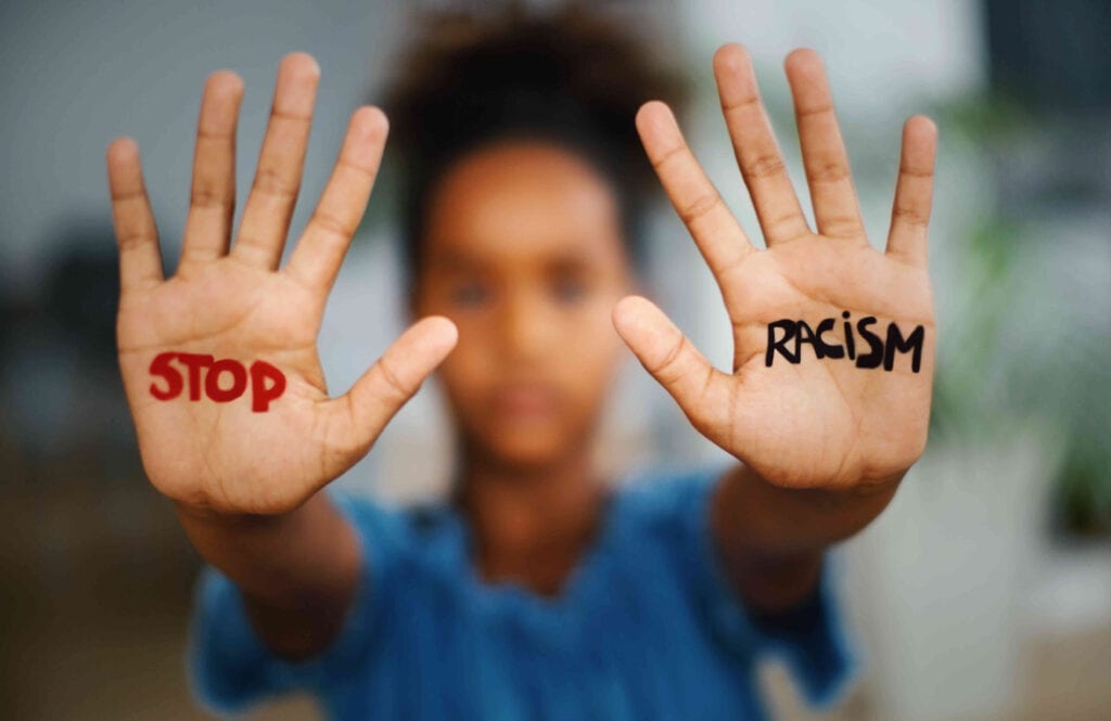 A person holding up their hands with the words “stop racism” written on each palm